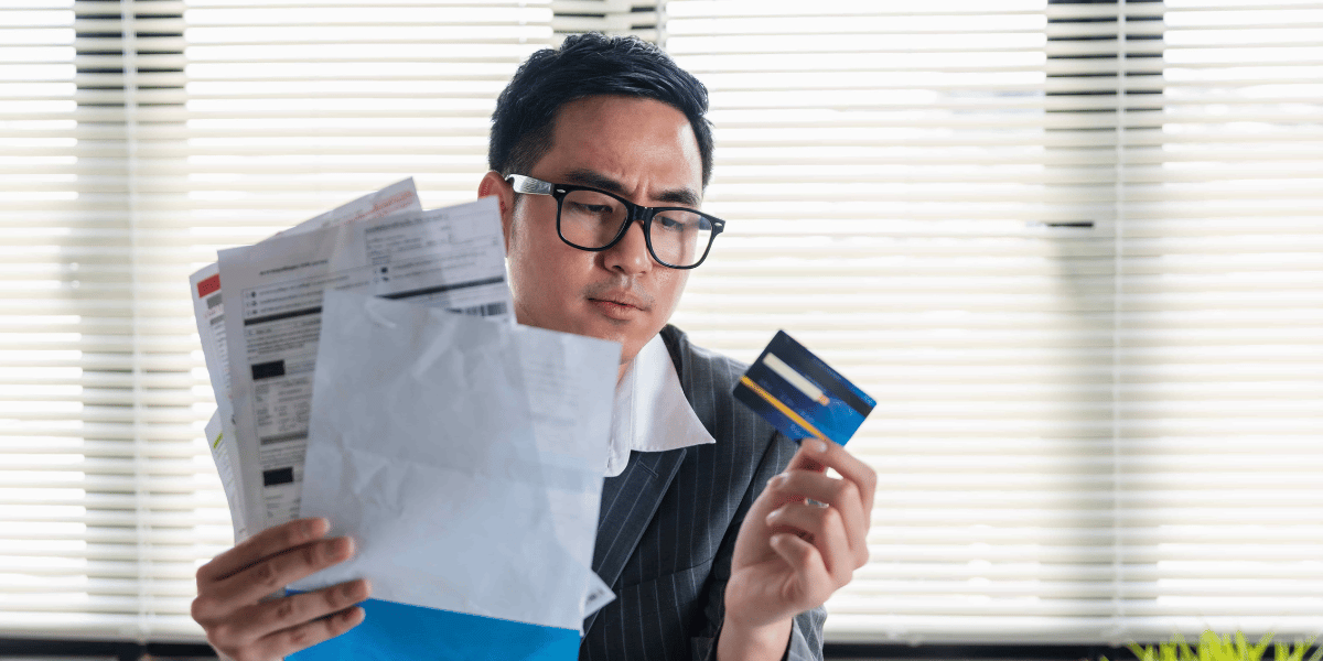 Stressed young asian businessman holding so many expenses bills electricity bill,water bill,internet bill,cell phone bill and credit card bill in his hand no money to pay debt